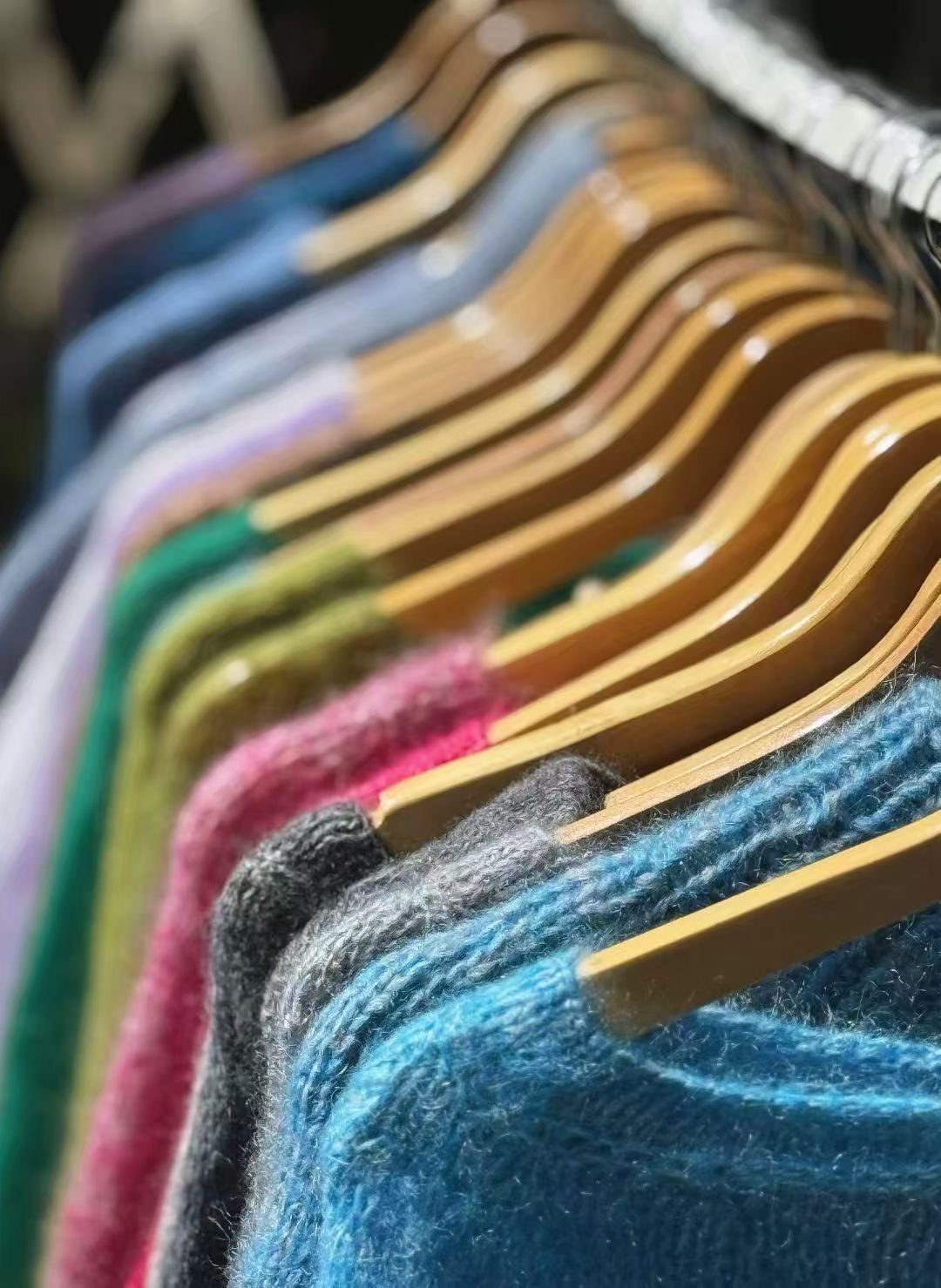 A row of hand-knit mohair sweaters in vivid colour, on hangers